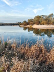 Autumn landscape on the river with blue sky and dry field grass.