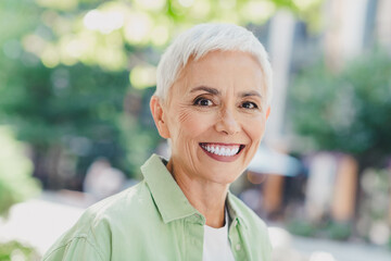 Confident elderly woman smiles outdoors in casual green shirt on a sunny day urban life cityscape...