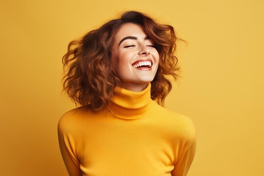 Happy young woman with curly hair wearing a yellow turtleneck laughing cheerfully on a yellow background