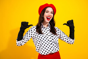 Happy fashion woman in red beret and polka dot blouse posing confidently against a bright yellow background