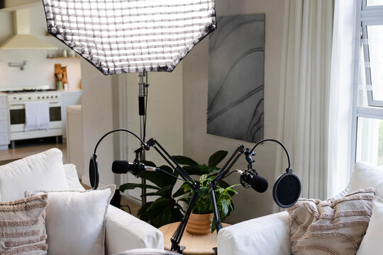 Two boom arms are holding mics with pop filters on round table between sofas, softbox lighting