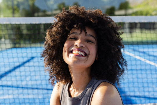 African American woman smiling while standing on blue hardcourt in sleeveless athletic top near net