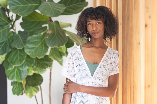 African woman standing at home by fiddle-leaf fig and wooden slat wall, wearing lace dress