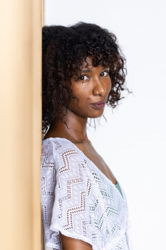 African woman leaning against beige wooden panel at studio, wearing white lace and green camisole