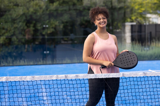Adult African American woman standing on court holding paddle pink top and leggings net, copy space