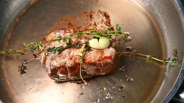 Beef steak searing in a stainless steel pan with garlic and thyme, showcasing the cooking process and rich textures of the meat and herbs