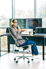 Smiling woman programmer working from home office with multiple monitors, coding and enjoying...