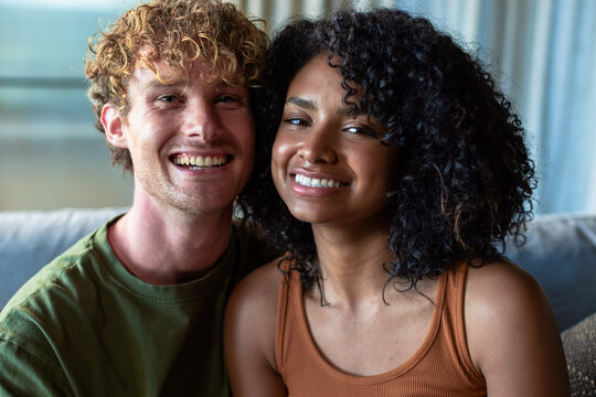 Couple sitting on couch in living room, smiling, wearing green T-shirt and rust tank with cushion