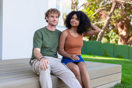Couple sitting on wooden deck at house, wearing green T-shirt and rust tank top