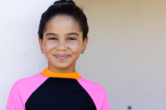 Teenage girl standing facing camera by pale wall wearing long-sleeve neon athletic top and hoops