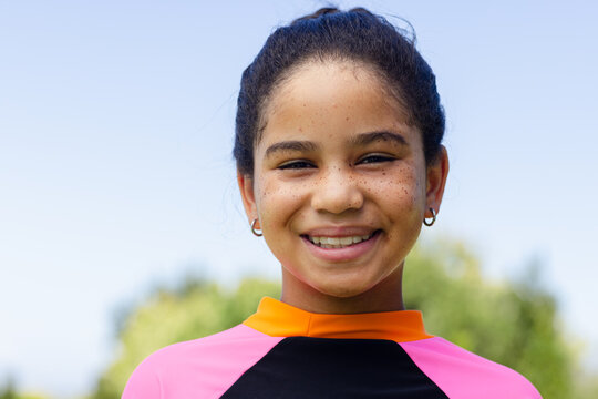 African American teenage female smiling while wearing bright athletic top and hoop earrings at park