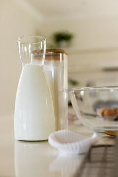 Glass carafe is sweating with milk droplets on glossy counter, jar, eggs, liners nearby
