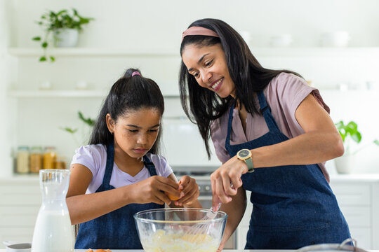 African American mother and child in blue aprons mixing batter at kitchen counter with glass bowl