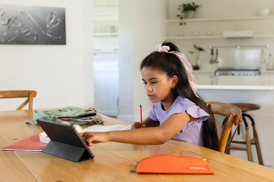 Teenage African American female sitting at table using tablet and pencil, lavender top, copy space
