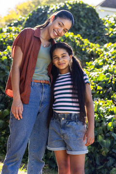 African American female mother and child standing, leaning and smiling in sunlit yard with necklace