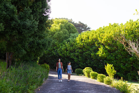African female family mother in rust coat and teenage daughter in striped shirt walking gravel path