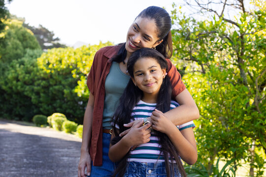 African American mother and child hugging standing in sunny yard near paved path bracelet visible