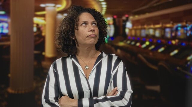 Woman wearing striped shirt crossing arms in front of illuminated slot machine row at casino; rejection.