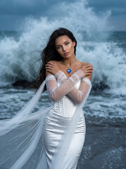 Young woman posing by the sea in a white dress with flowing fabric  
