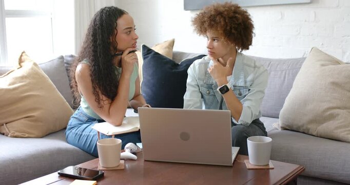 Two African American women, left speaking while holding notebook and pen, right typing on laptop