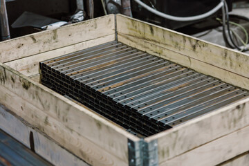 Metal profiles and steel parts stored in a wooden crate in an industrial warehouse.
