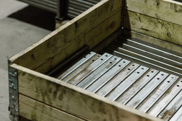 Metal profiles and steel parts stored in a wooden crate in an industrial warehouse.
