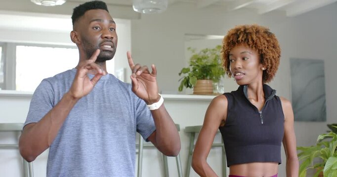 Diverse pair, man showing breathing for warmup in kitchen after cue, woman following, smartwatches