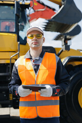 Industrial worker male holds tablet computer on background of production of excavator factory.