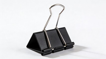 features a close-up of a black binder clip, a common office supply item. The clip is positioned upright against a plain white background, emphasizing its metallic and matte black surfaces. The clip's 