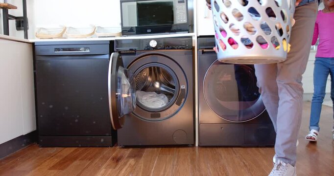 African American man carrying basket, loading washer for washing, youth female watching, copy space