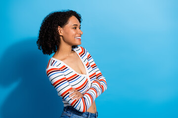 Young chic woman with curly hair smiles in a striped sweater against a bright blue background...