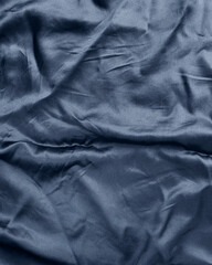 Crumpled blue satin fabric texture background. Luxury wavy dark blue silk material with soft light...