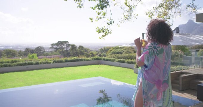 Sun drawing woman in pastel cover-up toward infinity pool edge, lifting glass, sipping, copy space