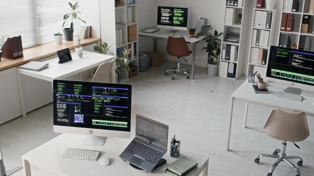 High angle shot of IT office workspace with minimalistic open plan interior featuring developer stations with computers displaying algorithmic code on multiple screens