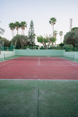 Obraz premium Empty tennis court with red surface and palm trees