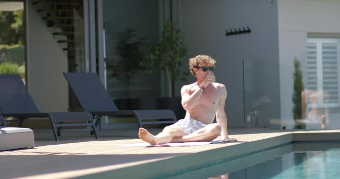 Man mid-20s feeling warm, sipping bottle while sitting cross-legged on towel at pool deck