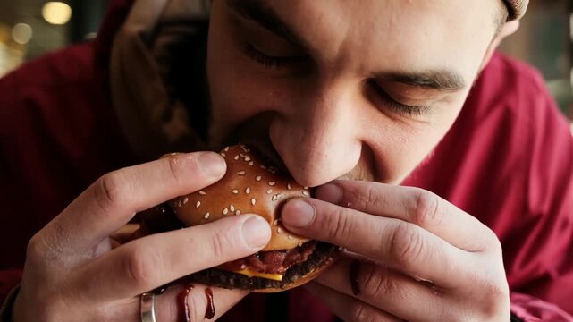 Close up of a man holding and eating a burger with sesame bun in a restaurant. Concept of fast food culture, casual dining and enjoying a meal