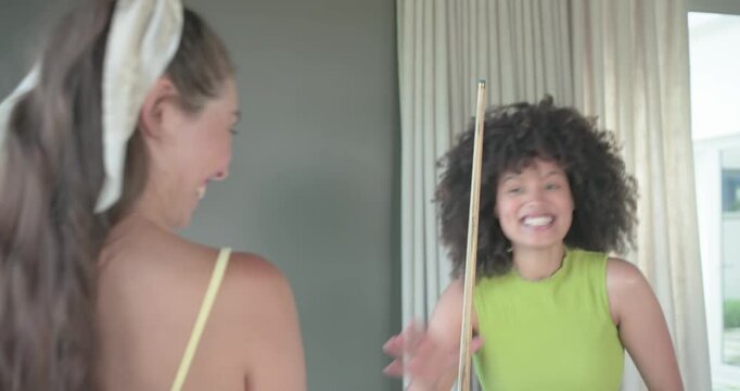 Diverse female friends exchanging cues and taking shots on pool table in rec room for fun