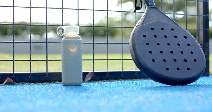 Neon tennis ball entering from right, bouncing, rolling past water bottle to paddle on blue court