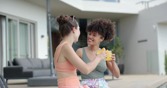 Diverse female friends exchanging smiles, raising orange-slice glasses, toasting friendship on deck