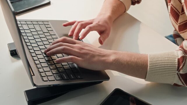 High angle shot of unseen male software developer writing commands on laptop computer while working at desk in brightly lit office