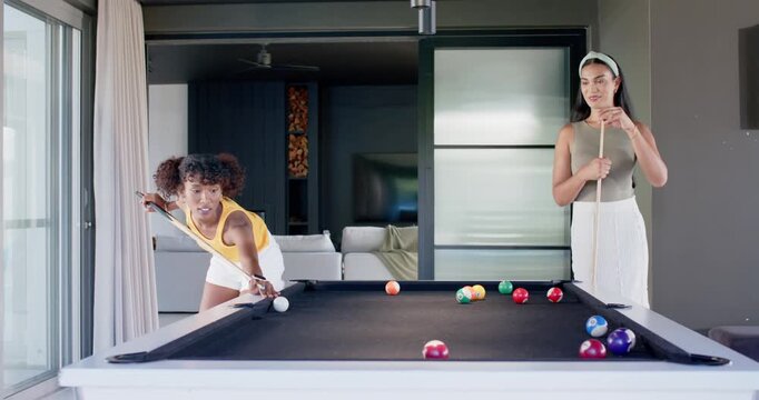 African American friends playing pool at home, left woman aiming and striking cue ball to win