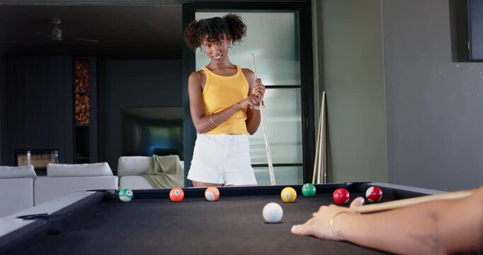 African American friends at home playing pool friend striking cue ball woman in yellow top watching