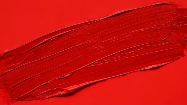 A vibrant red smear of lip gloss on a matching red background with white space