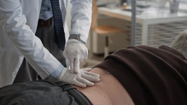 Cropped shot of unrecognizable gloved urologist tapping and palpating patient lower back during physical examination in modern medical office