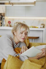 Mature woman reading book on yellow sofa at home