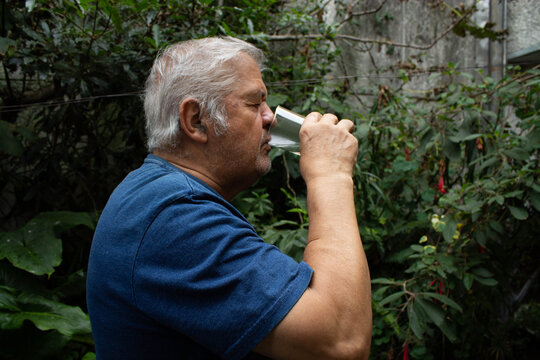 Hombre bebiendo un vaso de agua pura al aire libre en un jard&iacute;n frondoso.