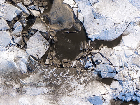 Aerial view of a stark, fractured ice landscape meeting dark, still waters, creating a mesmerizing dance of light and shadow near the Vistula River, Warszawa, Masovian Voivodeship, Poland.
