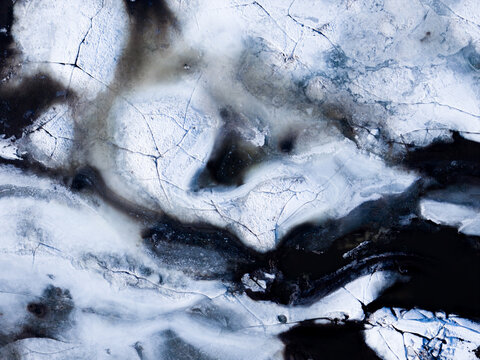 Aerial view of the frozen Vistula River, its icy surface fractured into jagged patterns of white and dark hues, creating a stark winter landscape, Warszawa, Masovian Voivodeship, Poland.