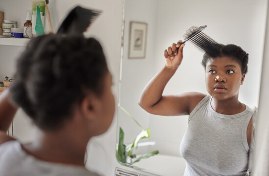 Young African woman trying to style her hair in a bathroom mirror